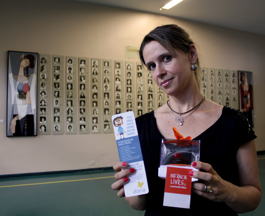 Foto de uma mulher segurando um panfleto e um presenta do Instituto Alana.