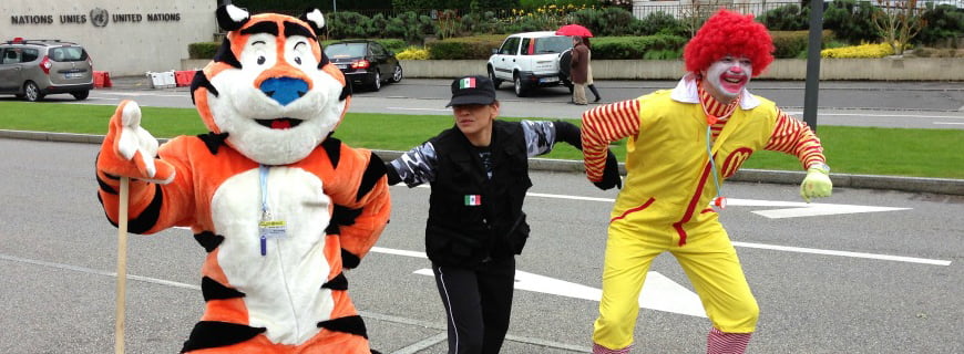 Foto de uma guarda segurando duas mascotes, um da empresa McDonald's e outra da Sucrilhos.