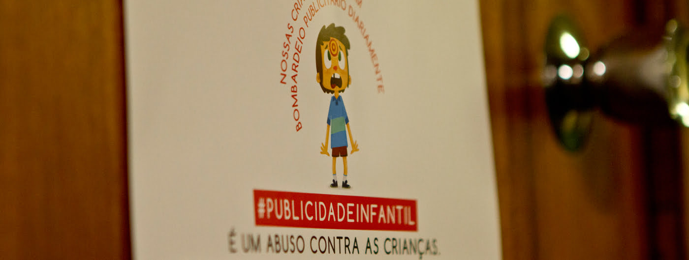 Foto de um cartas com um desenho de um garoto assustado olhando para um alvo em sua testa descreve: Publicidade infantil é um abuso contra as crianças.