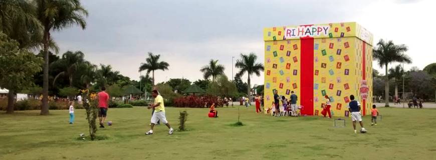 Foto pessoas caminhando em um parque com uma caixa gigante de presente da Ri Happy.