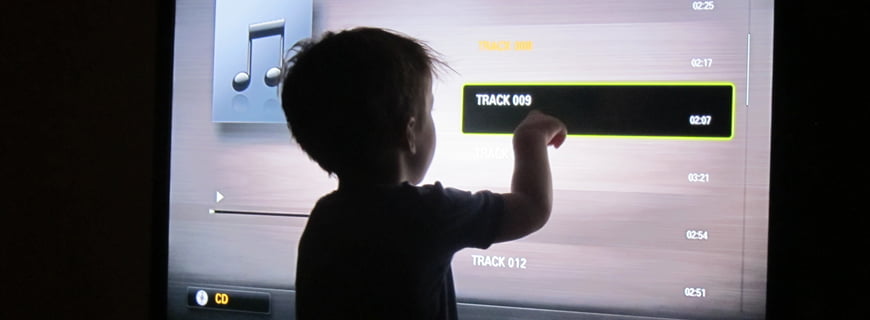 Foto de um garoto apontando para uma faixa de musica de uma televisão.
