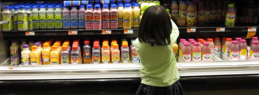 Foto de uma garota em frente a uma prateleira de supermercado com tipos de bebidas diferentes.