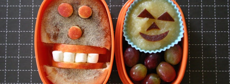 Foto com duas lancheiras, os alimentos dentro da lancheiras formam rosto felizes.