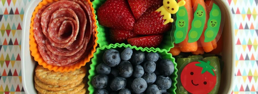 Foto de uma lancheira saudável com frutas, legumes, salame e bolachas.
