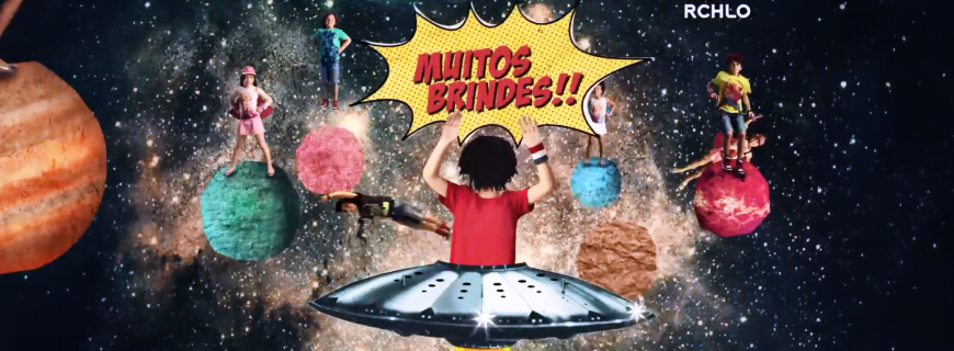Comercia promocional da Riachuelo, onde crianças em cima de planetas estão vestidas de super heróis, uma criança com um balão está gritando: Muitos Brindes!!!