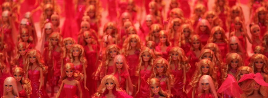 Foto com várias bonecas de plástico com penteados diferente, todas são loiras e usam um vestido vermelho.