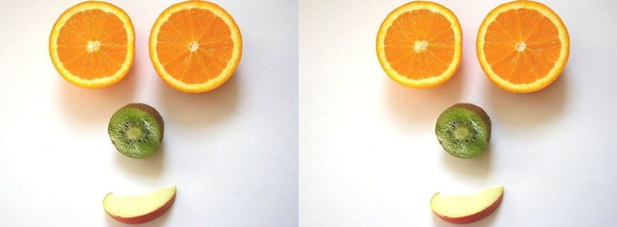Foto se repete duas vezes: Uma laranja cortada ao meio faz o formato de dois olhos, metade de um Quiuí forma um nariz e uma maçã forma uma boca.