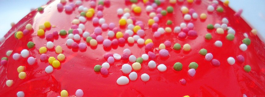 Foto de um doce rosa com vários confeitos multicoloridos por cima do doce.