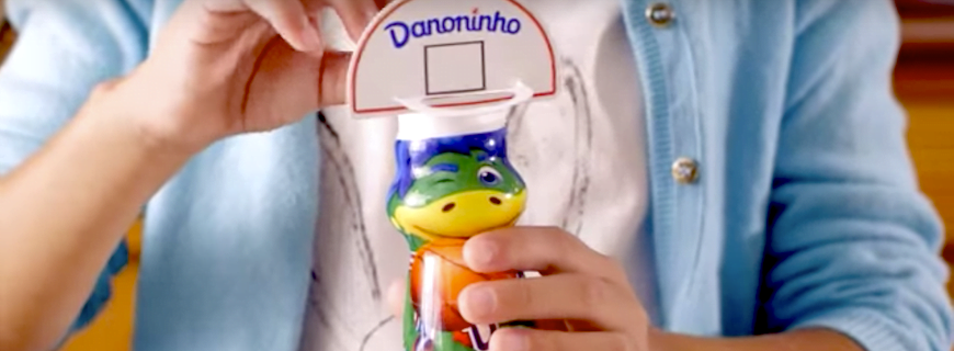 Foto comercial da Danone. onde uma pessoa está segurando a mascote Dino.