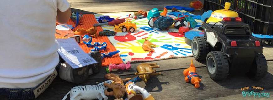 Foto de vários tipos de brinquedos espalhadas no chão, uma pessoa esta ajoelhada ao lado.