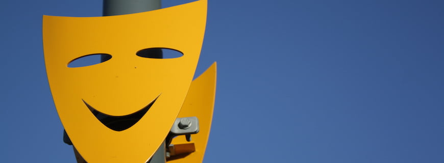 Foto de um poste com duas máscaras teatrais amarelas presa ao poste.