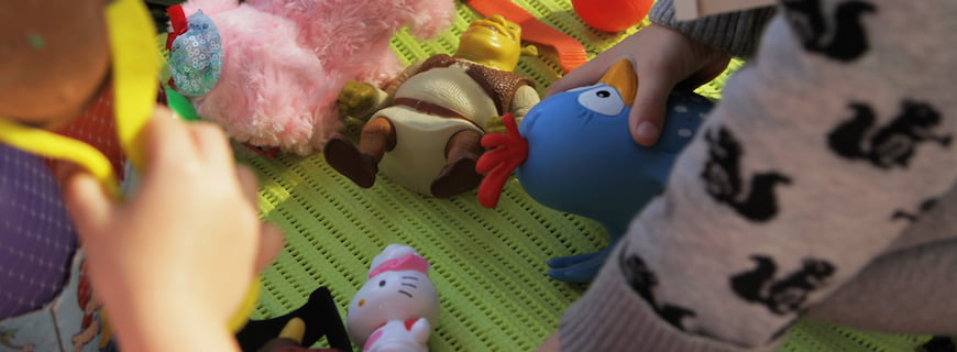 Foto de crianças brincando com brinquedos, há vários bonecos esparramados pelo chão.