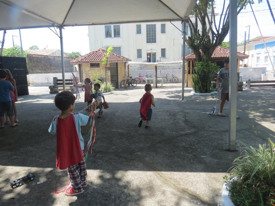 Crianças com capas vermelhas estão em uma praça ao ar livre e brincam com fios coloridos