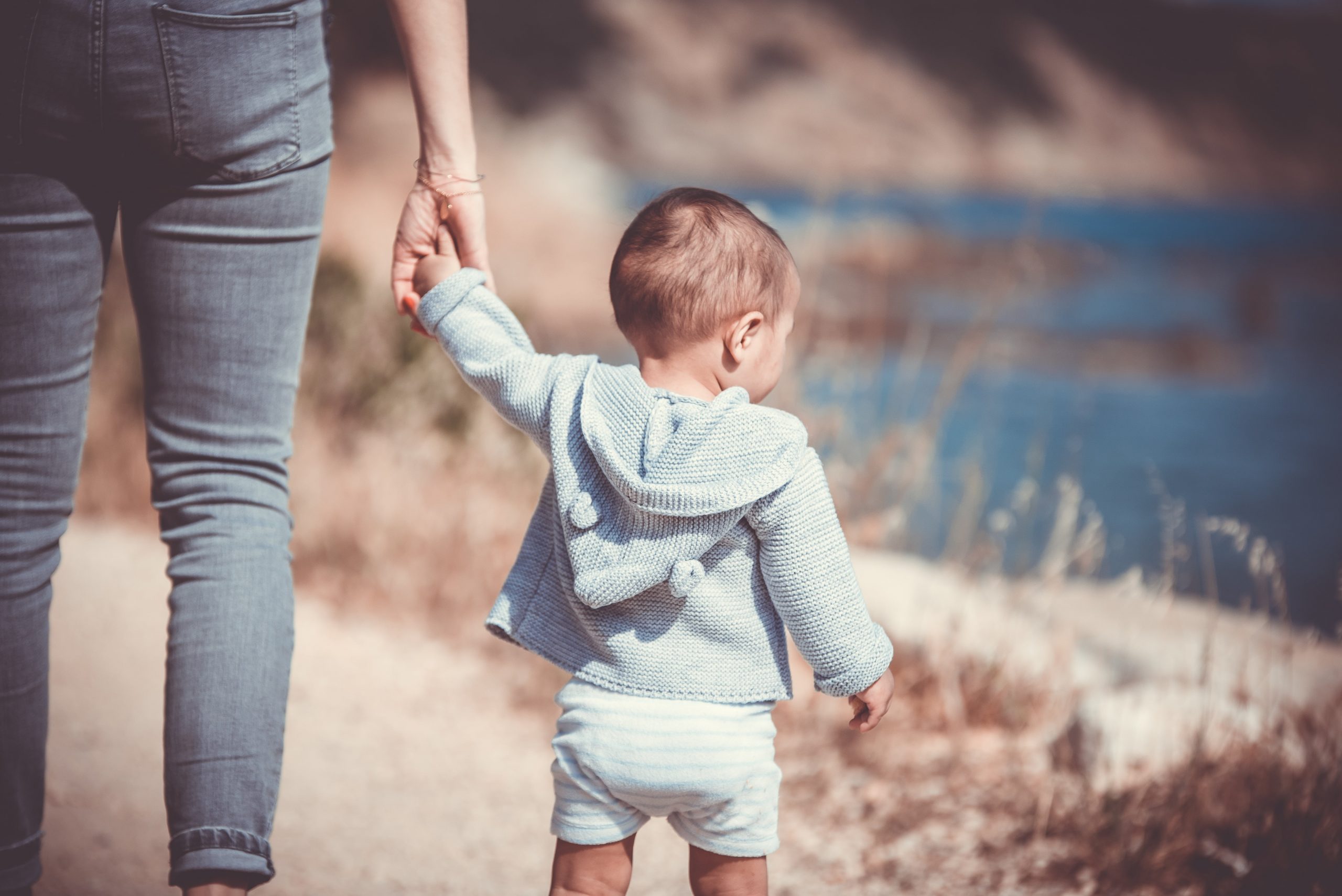 Foto de uma pessoa segurando a mão de um bebê que está em pé.