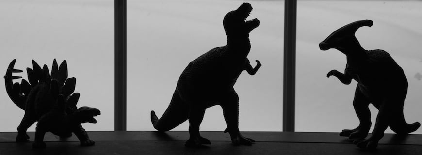 Foto preto e branca com a silhueta de três bonecos de dinossauros.