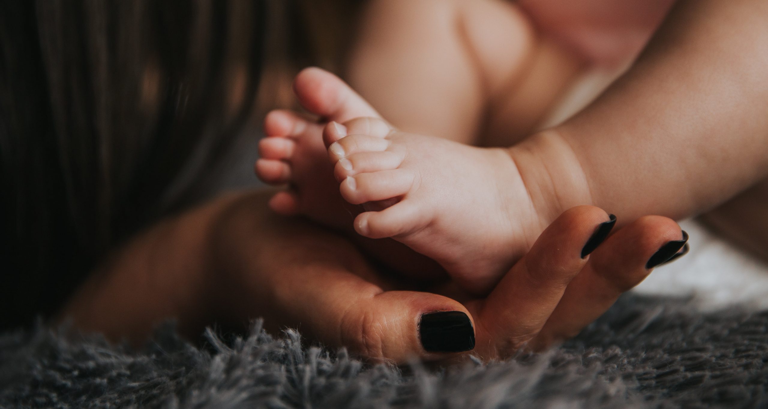 Foto de uma pessoa segurando pés de um bebê em uma mão.