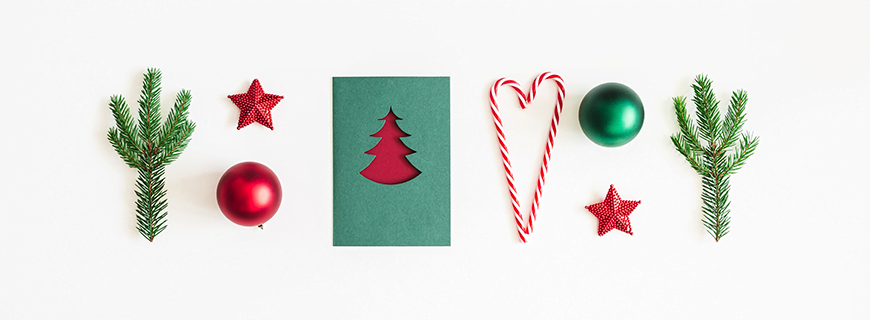 Foto com elementos natalinos em verde e vermelho: ramos de pinheiros, cartão de natal, enfeites de árvore