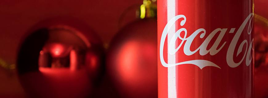 Foto de lata de Coca Cola. Ao fundo, bolas de enfeite de Natal vermelhas