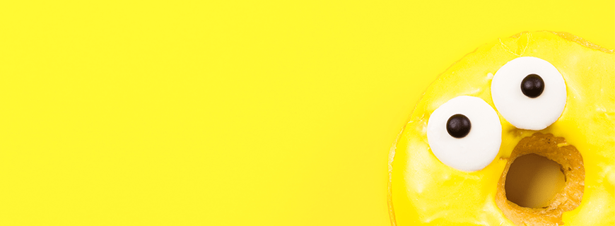 Em fundo amarelo, foto de uma rosquinha com cobertura amarela e olhos espantados