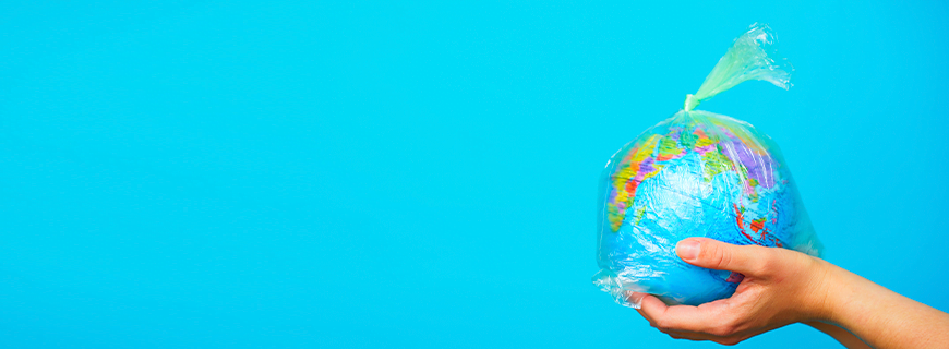 em fundo azul, mão segurando um globo terrestre dentro de uma sacola plástica fechada como imagem de apoio ao texto sobre a Semana Sem Plástico