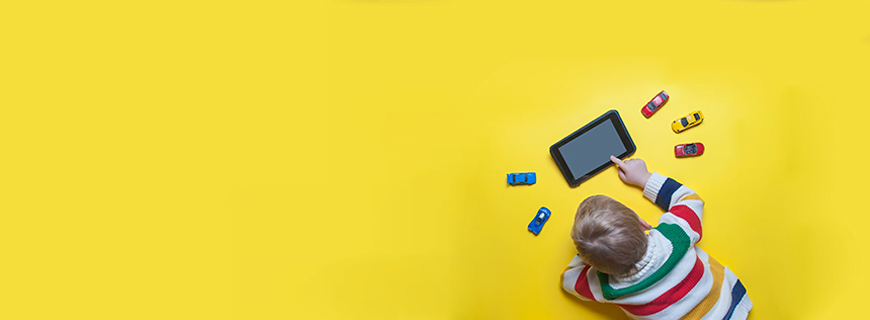 em fundo amarelo, foto de cima de uma criança deitada no chão brincando com um tablet e diversos carrinhos de brinquedo ao redor como imagem de apoio do texto sobre crianças no ambiente digital