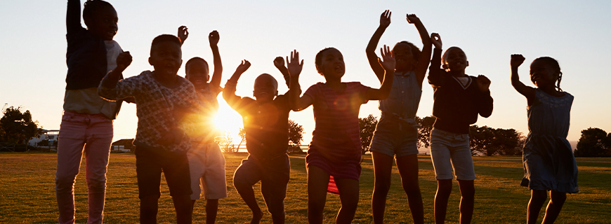 foto de diversas crianças em um campo aberto com o sol atrás delas e estão comemorando, pulando e com os braços para cima, como imagem de apoio ao texto sobre ben & jerry's