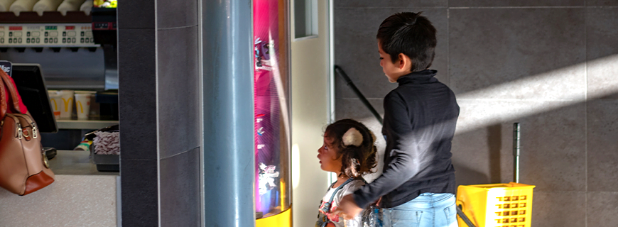 foto de duas crianças olhando para um totem com os brinquedos que vêm com lanches em uma rede de fast food como imagem de apoio ao texto sobre proibição de comercialização de brinquedos acompanhados de lanche