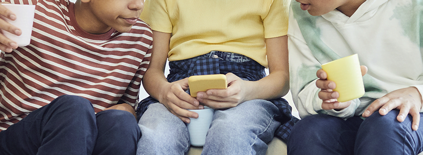 foto de três crianças sentadas, em que a do meio está segurando um celular e as duas outras estão olhando para o aparelho como imagem de apoio ao texto sobre maior proteção on-line infantil em todo o mundo