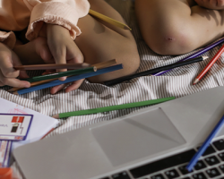 foto de duas crianças sentadas na cama brincando com lápis coloridos e um computador na frente como imagem de apoio ao texto sobre direitos digitais infantis na RightsCon
