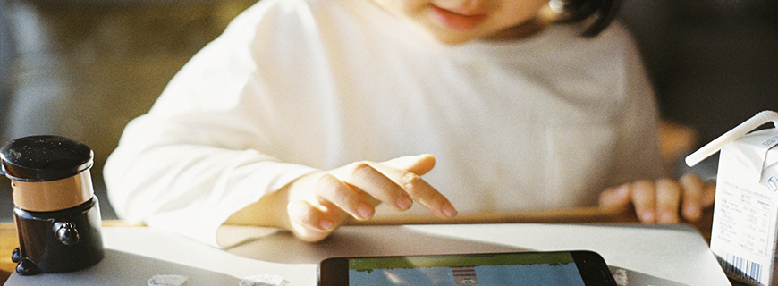 foto de uma criança de frente mexendo em um celular em cima de uma mesa como imagem de apoio do texto sobre produção digital de qualidade para crianças e adolescentes
