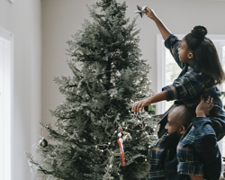 foto de uma criança sendo segurada pelo pai para botar a estrela em cima da árvore de natal como imagem de apoio para o texto sobre Natal com menos consumismo
