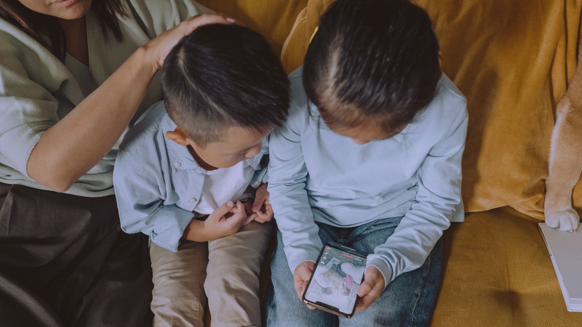 Na imagem, duas crianças usam um celular com um adulto responsável observando. A foto ilustra matéria sobre consulta pública sobre uso de telas realizada pelo Governo Federal.