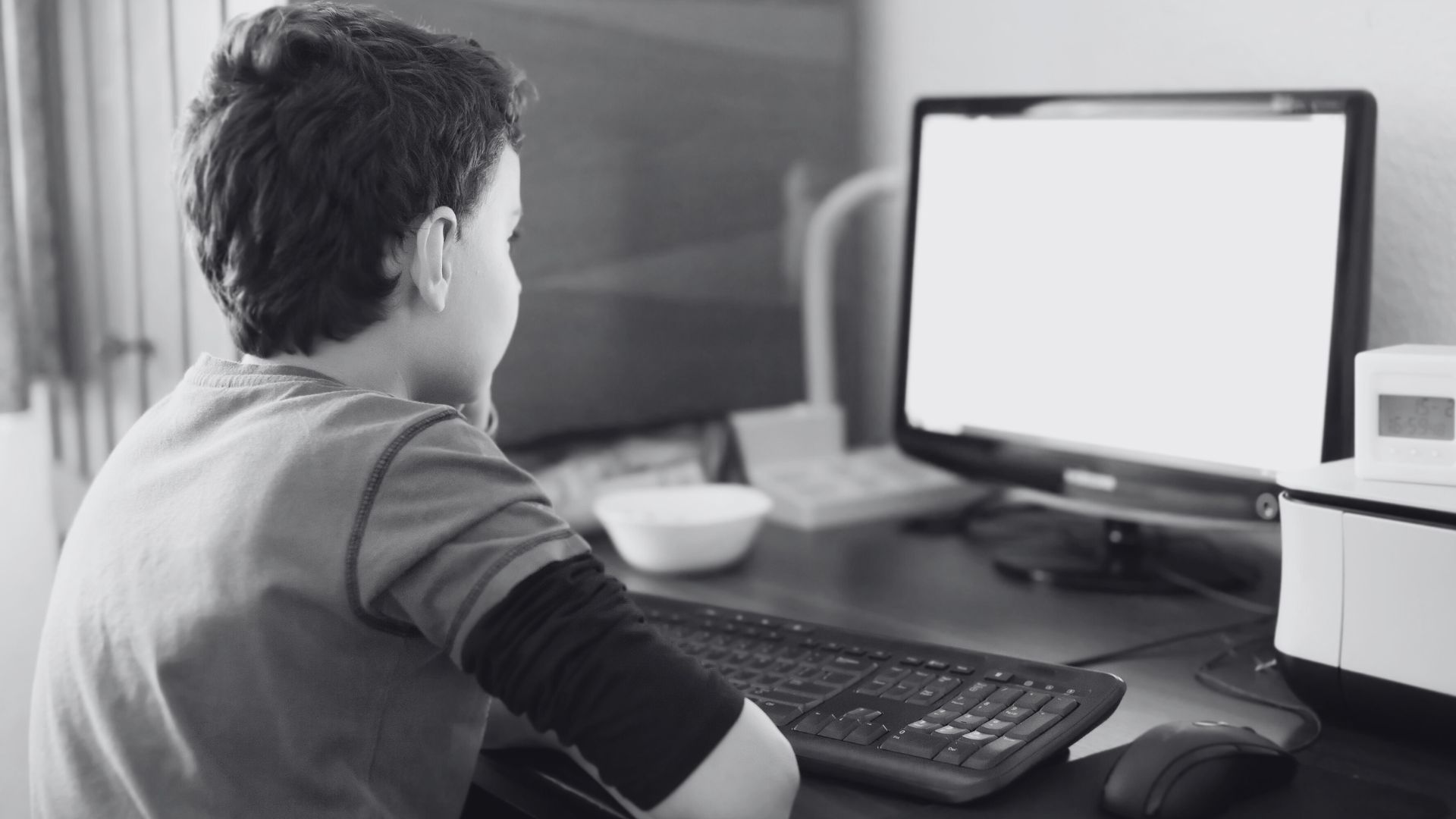Imagem em preto e branco de um menino de costas olhando para o monitor de um computador. A imagem ilustra matéria sobre denúncia realizada no Habbo, jogo de simulação virtual.