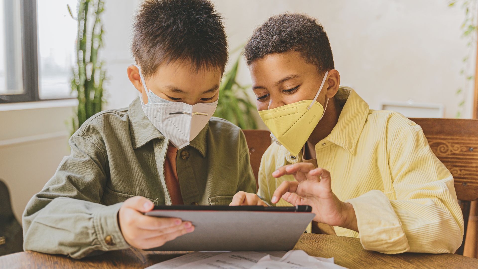 Uma criança de etnia amarela e outra negra olham para um tablet. Elas utilizam máscaras. A imagem ilustra matéria sobre lançamento de cartilhas voltadas à defesa de crianças e adolescentes na Internet.