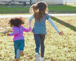 Duas meninas estão de costas e correm de mãos dadas em um jardim. A imagem ilustra matéria sobre a aprovação da resolução do Conanda.